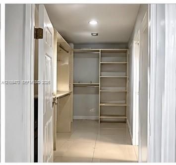 Walk-in closet featuring light-toned tile flooring, built-in open shelving units, and integrated hanging rods