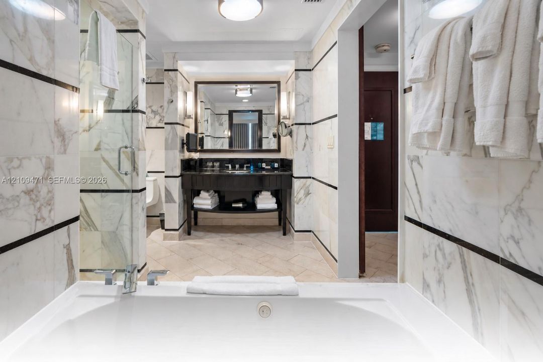 Stone-surround soaking tub, glass-enclosed shower, stone-tiled walls with decorative inlay, dark-finish vanity with countertop sink, and recessed lighting