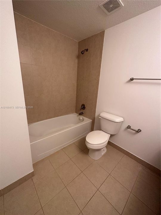 Full bathtub featuring ceramic tile surround, ceramic floor tiling, white plumbing fixtures, and brushed metal hardware