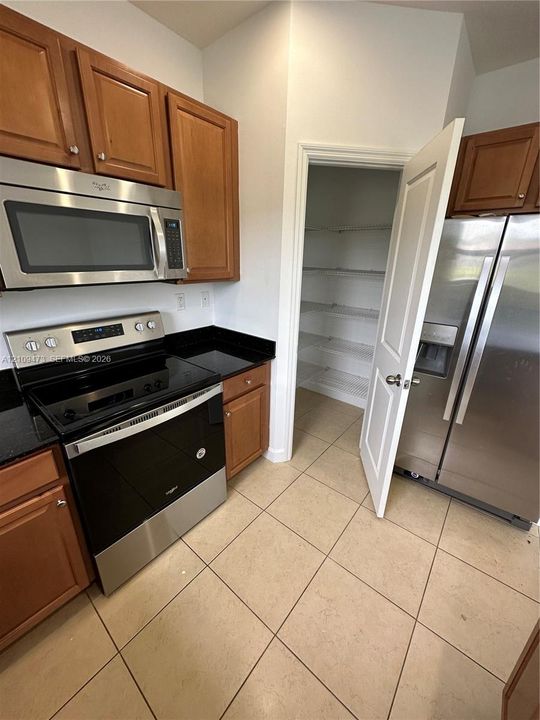 Kitchen featuring natural wood cabinetry, stone countertops, stainless steel appliances, tile flooring, and a walk-in pantry with wire shelving