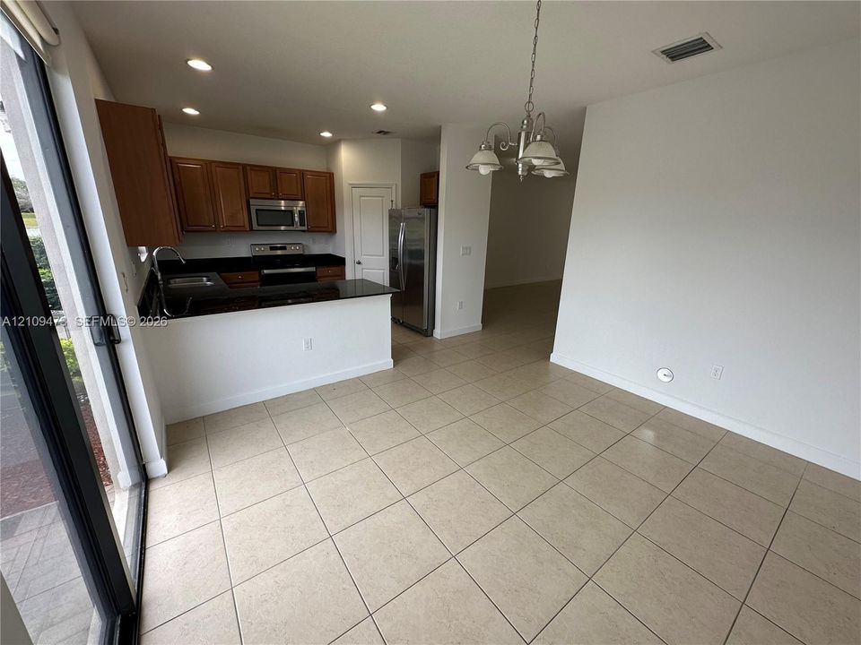 Kitchen featuring dark-toned stone countertops, stainless steel appliances, wood cabinetry, recessed lighting, and tile flooring
