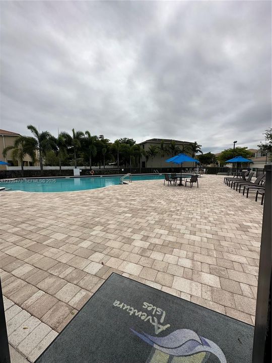 Community swimming pool featuring a paved deck and surrounding palm trees