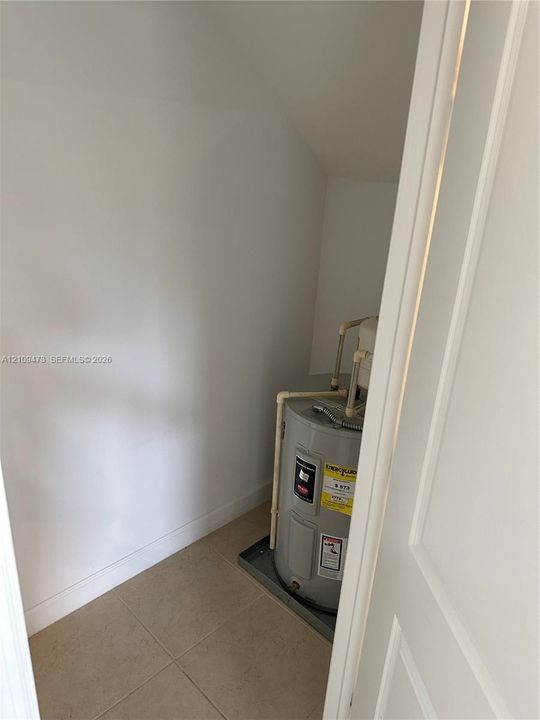 Utility closet featuring tile flooring, smooth white walls, and a dedicated water heater unit