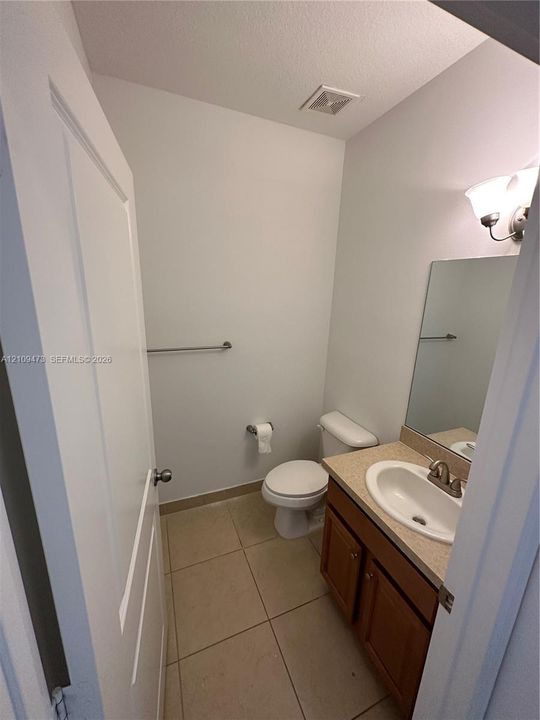 Bathroom featuring ceramic tile flooring, wood-finish vanity with a neutral solid-surface countertop, integrated basin, and wall-mounted vanity mirror