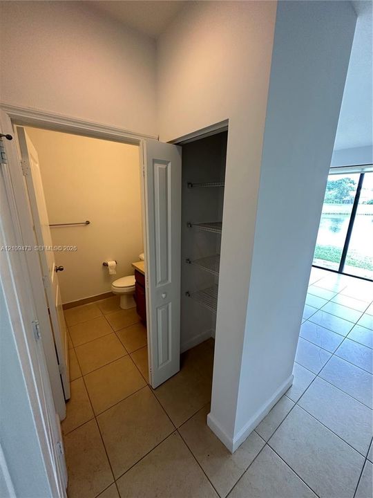 Interior hallway featuring ceramic tile flooring, a built-in closet with wire shelving, and a doorway to a restroom containing a vanity cabinet and toilet