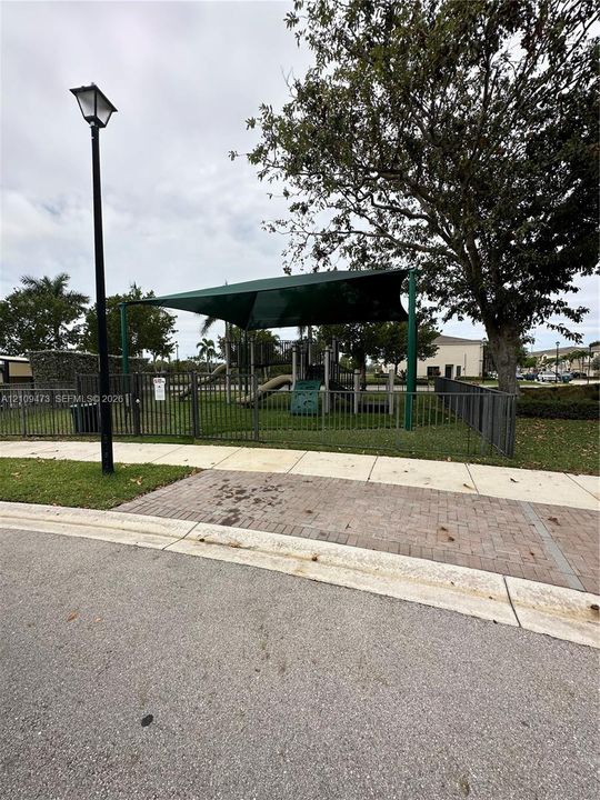 Outdoor recreation area featuring a fenced perimeter, shade canopy, integrated play structures, and mature landscaping