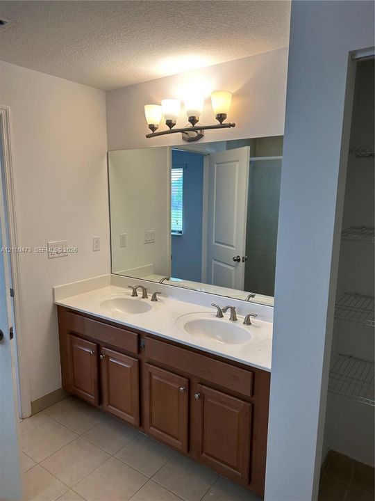 Dual-sink vanity featuring wood cabinetry, solid-surface countertop, metallic finish faucets, large wall-mounted mirror, and multi-light fixture
