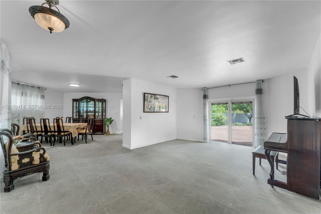Open-concept interior featuring large-format tile flooring, sliding glass doors, neutral wall color, and a semi-flush mount light fixture