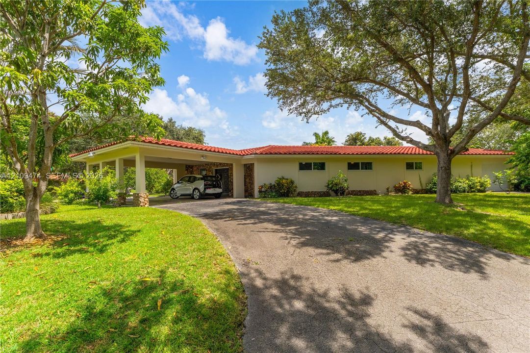 Single-story residence featuring a terracotta-tiled roof, covered carport, stone-clad exterior accent, and paved driveway situated on a landscaped lot