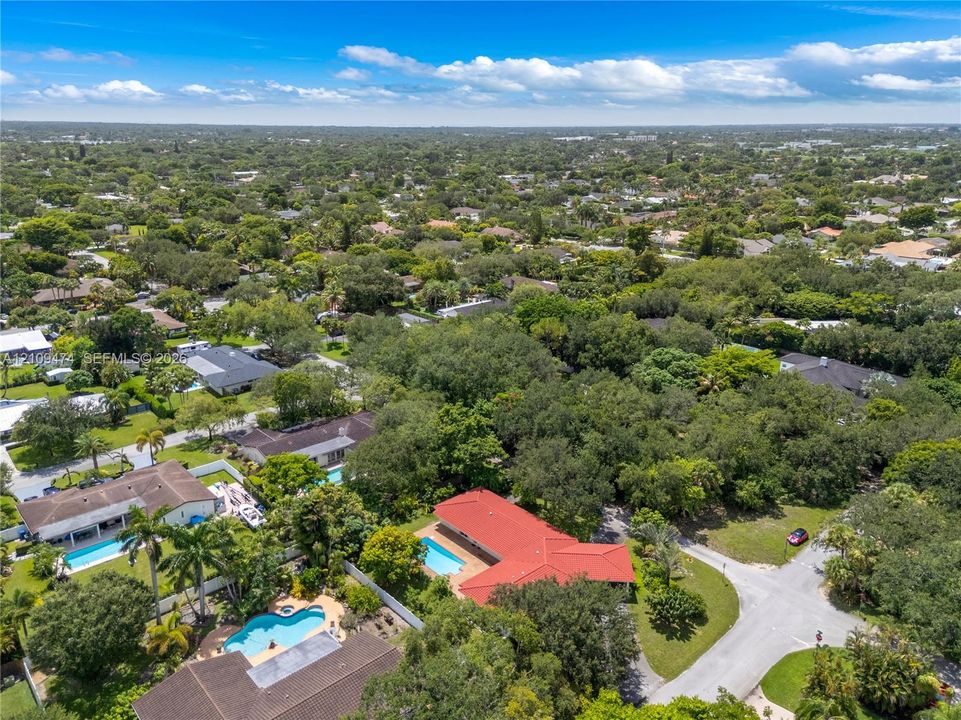 Aerial perspective featuring a residential property with a red tiled roof and a private swimming pool, surrounded by mature trees and lush vegetation