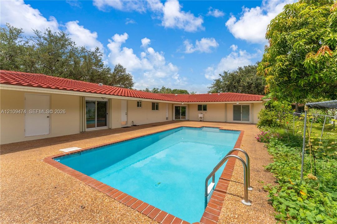 In-ground swimming pool with brick coping, expansive aggregate patio, and red tile roof