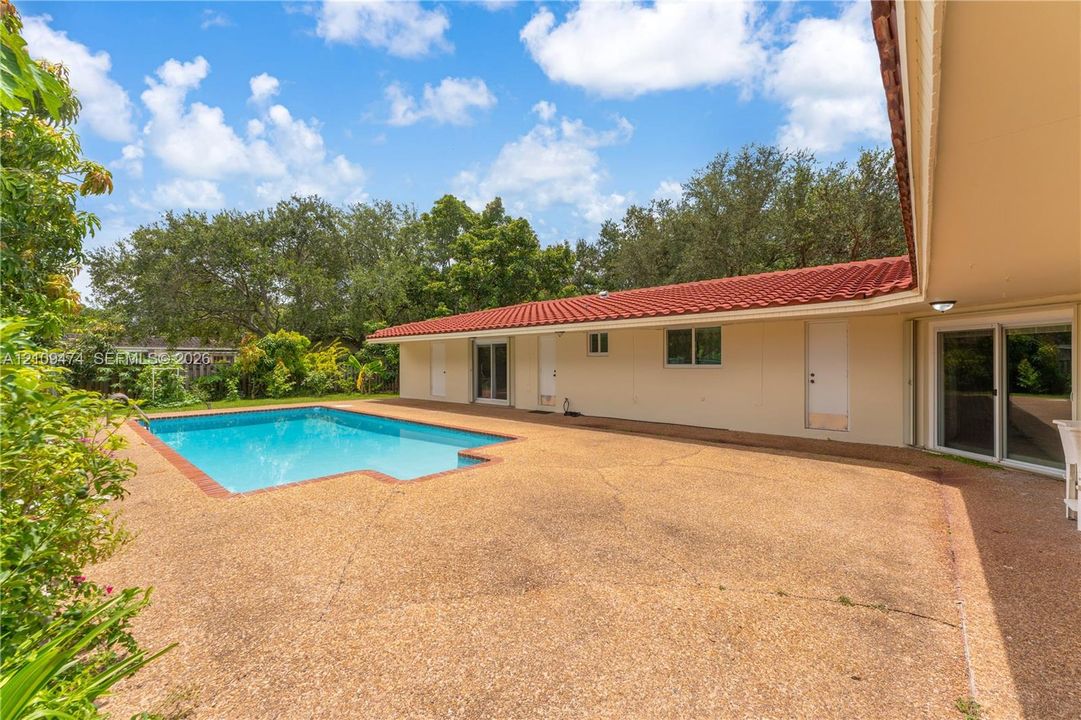 In-ground swimming pool featuring a red brick border, expansive aggregate patio, red tile roof, and multiple glass sliding door entries