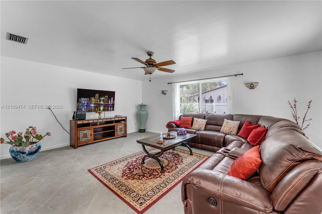 Living area featuring large-format ceramic tile flooring, a ceiling fan, sliding glass doors, and dual wall-mounted light fixtures
