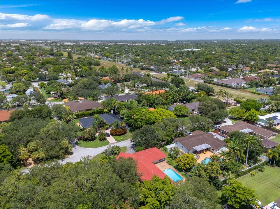 Aerial perspective showcasing a residential lot with a red tile roof, rectangular swimming pool, and dense mature tree canopy