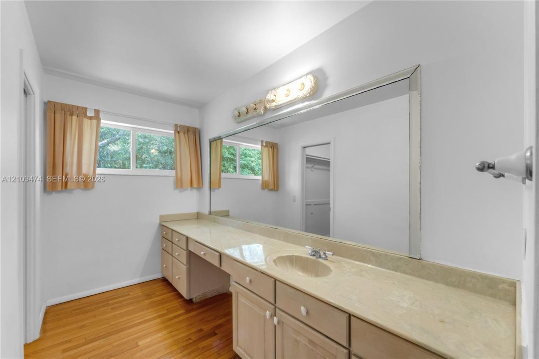 Extended vanity with solid-surface countertop, integrated basin, large-format wall mirror, and wood-finish flooring