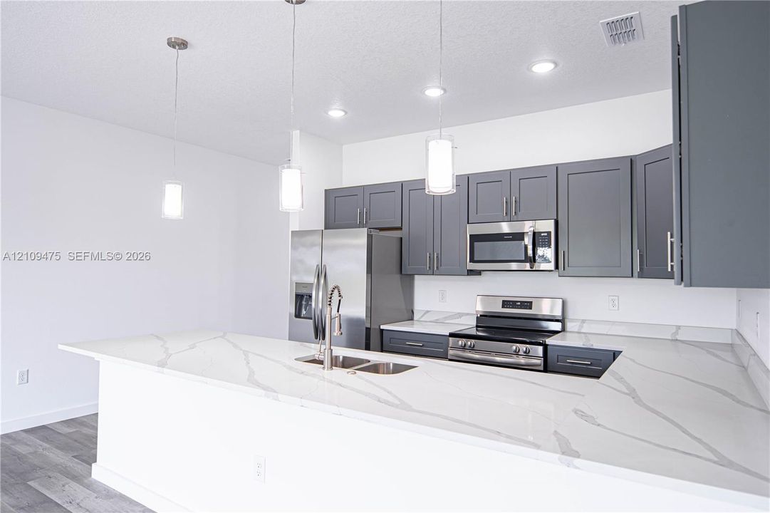 Kitchen featuring grey shaker-style cabinetry, white countertops with grey veining, stainless steel appliances, pendant lighting, and wood-finish flooring