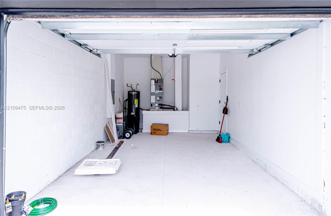 Enclosed garage featuring painted concrete block walls, concrete flooring, overhead door track system, and dedicated mechanical area with water heater