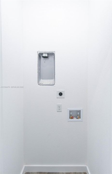 Utility hookup area featuring a recessed dryer vent box, dedicated 240-volt electrical outlet, standard electrical receptacle, and a recessed water supply valve box