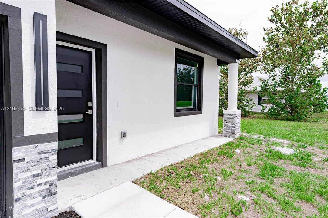 Modern exterior featuring white stucco finish, stacked stone accents, a multi-paneled dark entry door, and a covered porch supported by a cylindrical column
