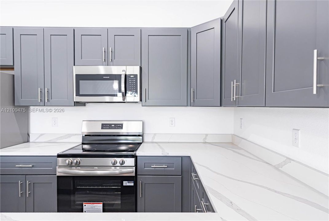 Kitchen featuring grey Shaker-style cabinetry, white countertops with integrated backsplash, and stainless steel appliances including a built-in microwave and range