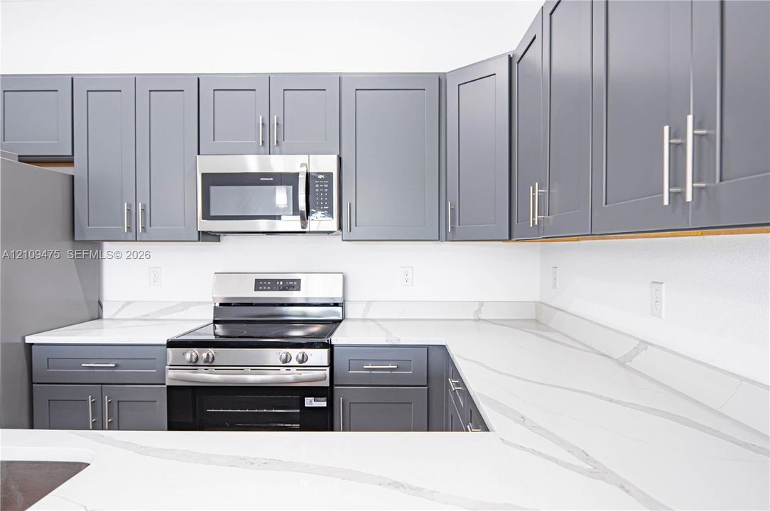 Kitchen featuring grey Shaker-style cabinetry, white stone-finish countertops with integrated backsplash, and stainless steel appliances