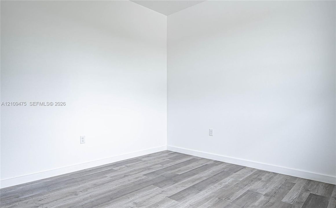 Neutral interior corner featuring smooth white walls and grey wood-finish flooring