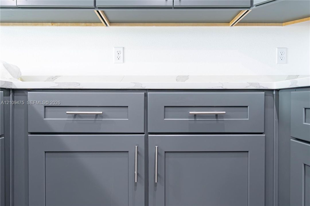 Shaker-style cabinetry finished in a slate grey tone, paired with a white stone-composite countertop featuring grey veining and brushed nickel hardware