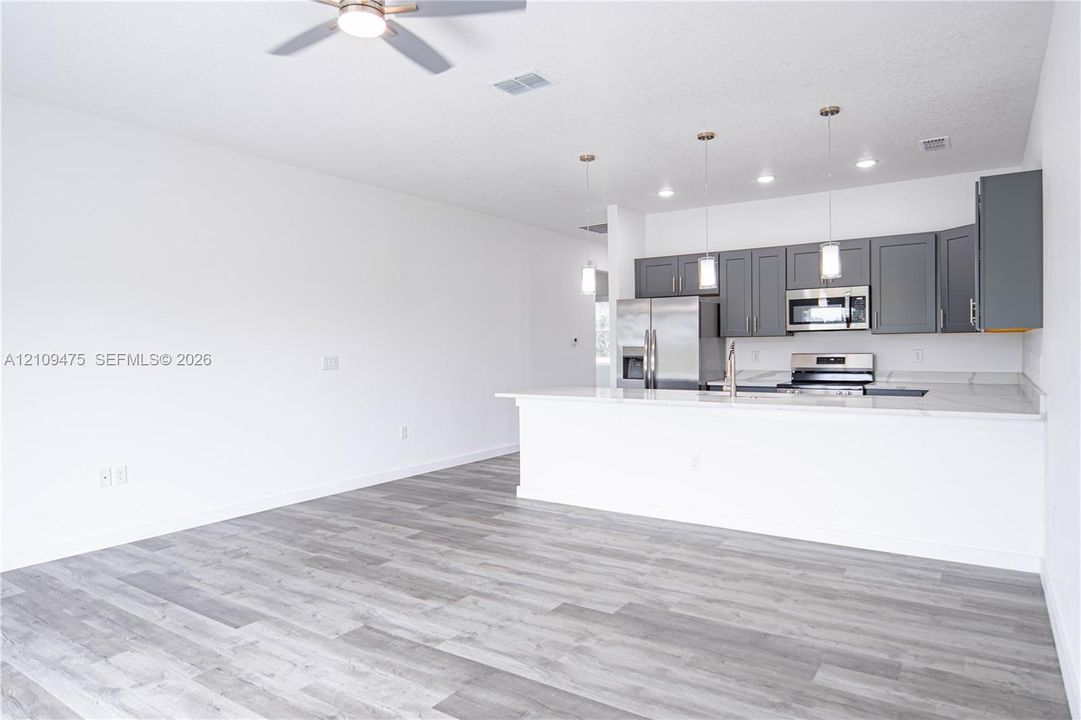 Kitchen featuring dark gray cabinetry, stainless steel appliances, a peninsula with stone-finish countertops, pendant lighting, and wood-finish flooring
