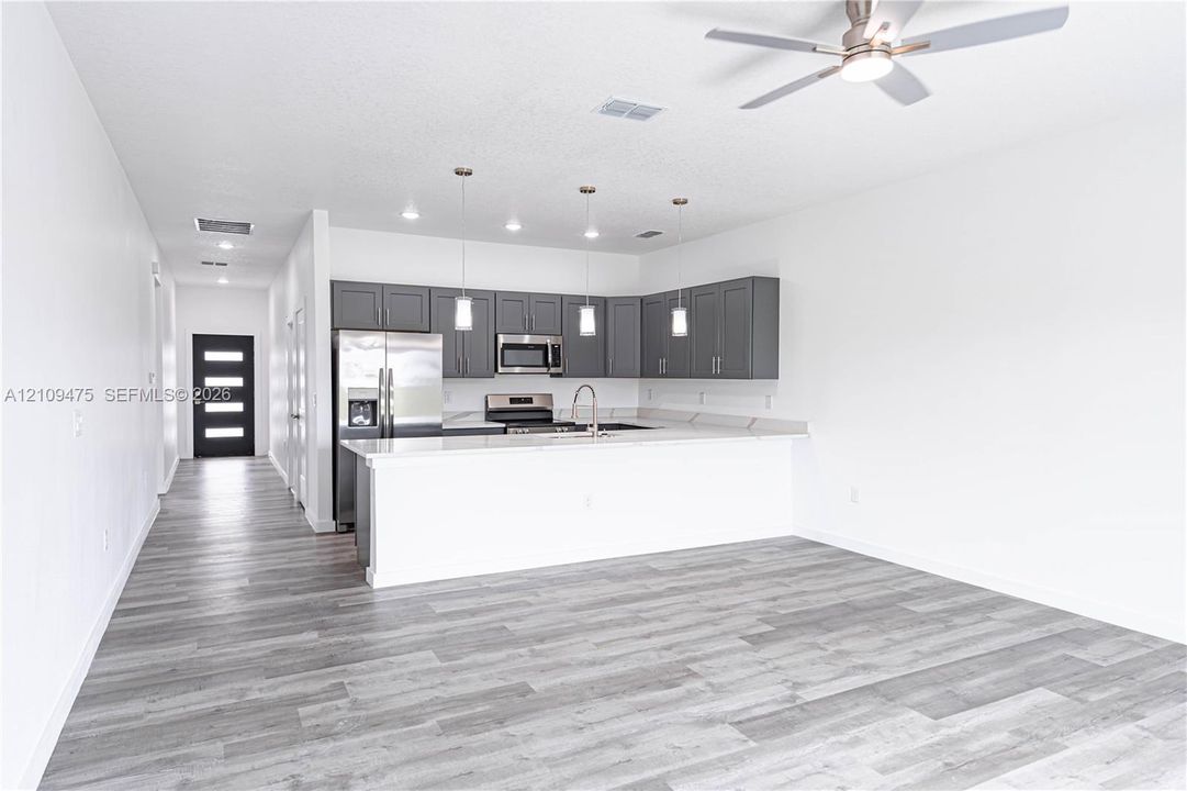 Open kitchen featuring grey cabinetry, quartz countertops, stainless steel appliances, pendant lighting, and wood-finish flooring