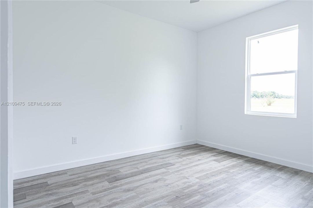 Neutral-toned interior space featuring crisp white walls, wood-finish flooring, and a single-hung window