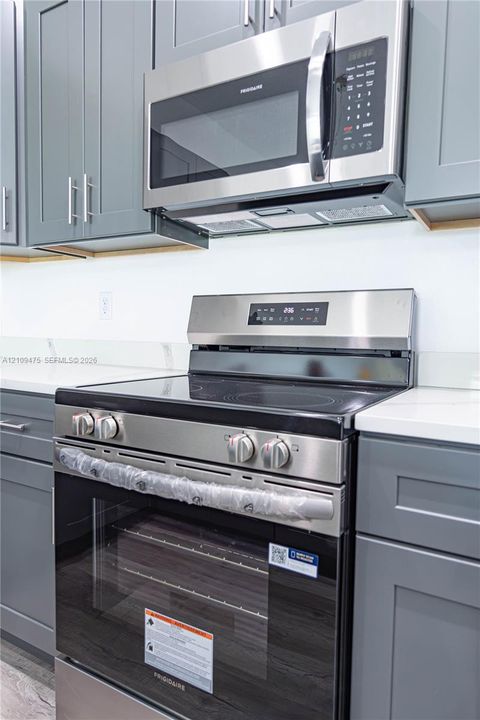 Stainless steel range with a glass cooktop, coordinating over-the-range microwave, gray shaker-style cabinetry, and solid surface countertops