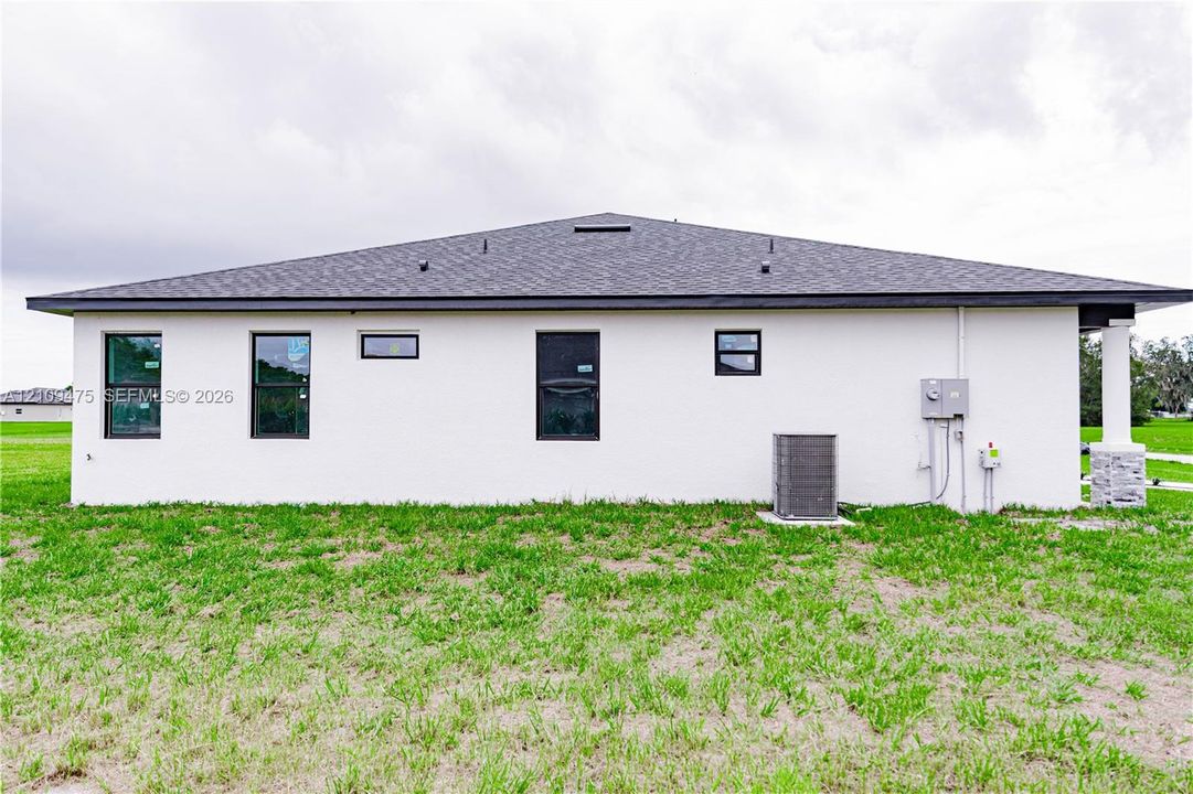 Stucco exterior featuring dark-framed windows, a hipped shingle roof, and stone-accented pillar