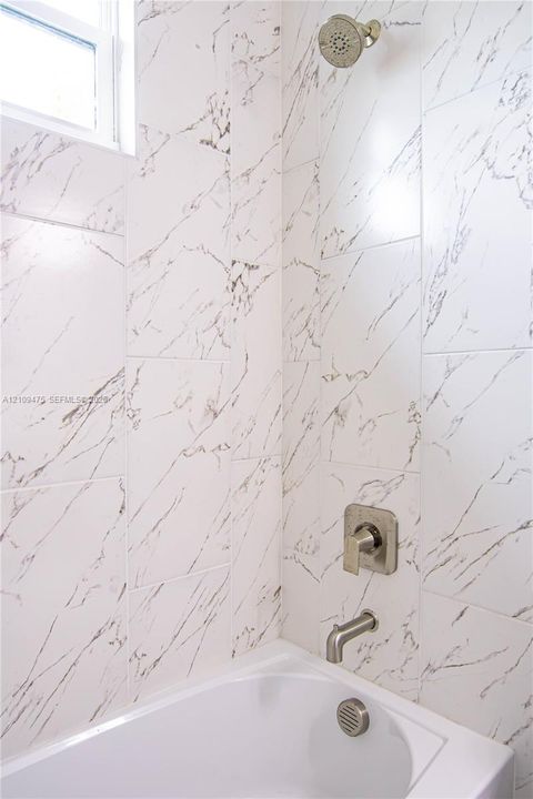 Shower enclosure featuring floor-to-ceiling white tile with charcoal veining, a wall-mounted showerhead, single-handle brushed nickel faucet, tub spout, and a rectangular window
