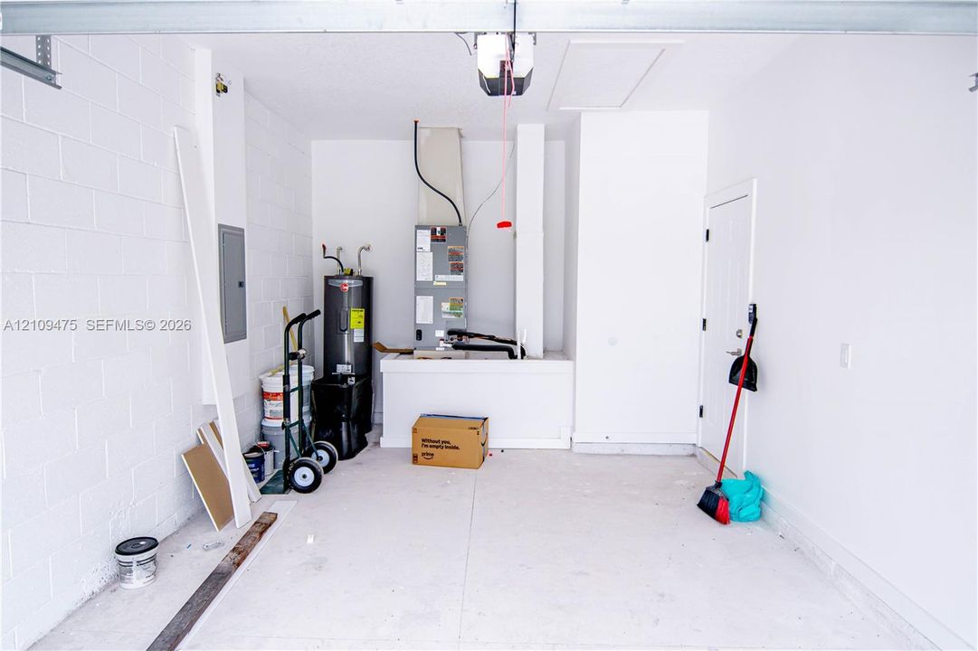 Garage space featuring painted concrete block walls, a concrete floor, an integrated electrical panel, and mechanical systems including a water heater and HVAC unit