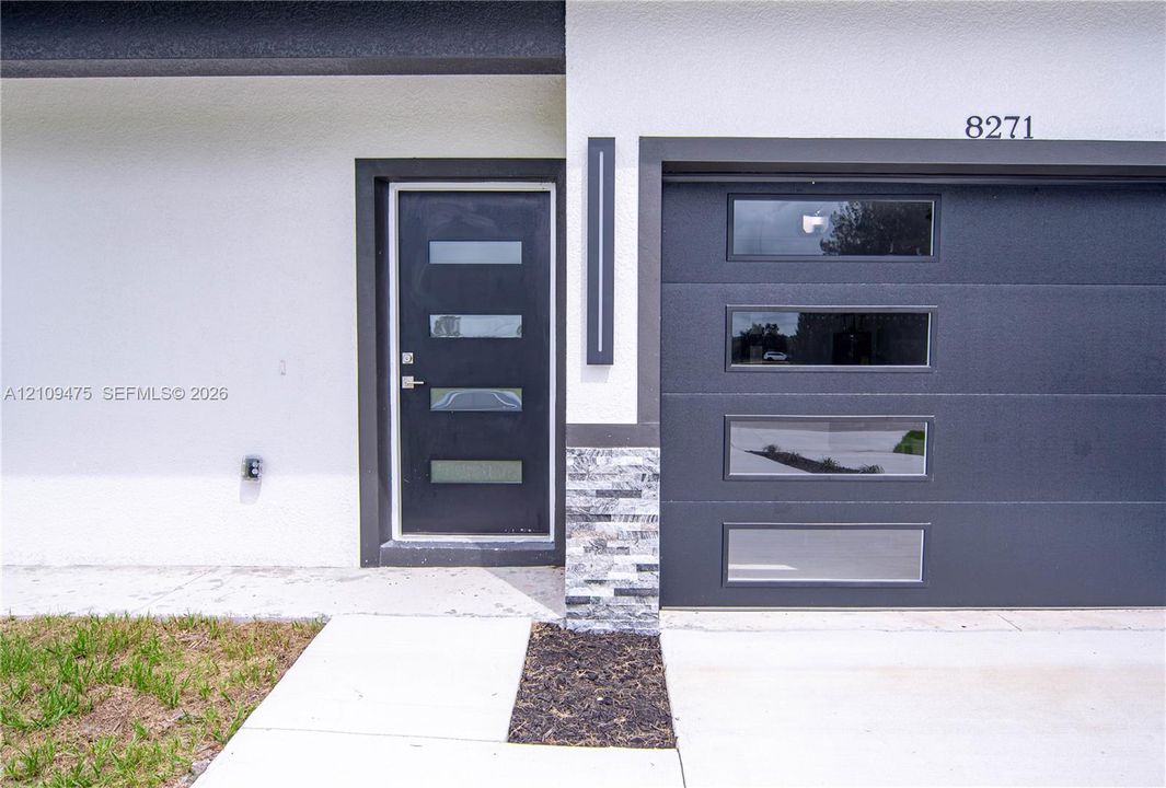 Modern facade featuring a stone veneer accent pillar, a dark-finish entry door with horizontal glass insets, and a matching garage door with rectangular window panels