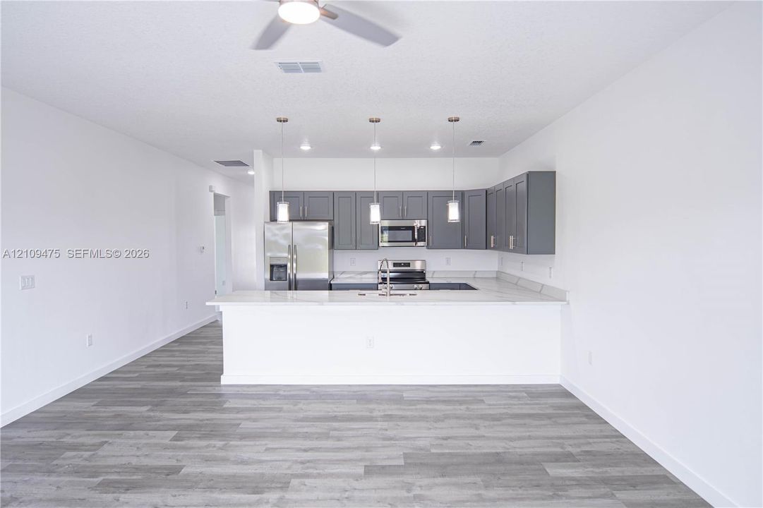 Kitchen featuring charcoal-toned cabinetry, light-toned countertops, stainless steel appliances, a breakfast bar, and wood-finish flooring