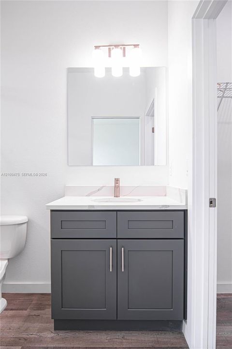Charcoal-finished vanity featuring shaker-style cabinetry, white stone-composite countertop with integrated sink, metallic faucet, and a modern three-bulb vanity light fixture