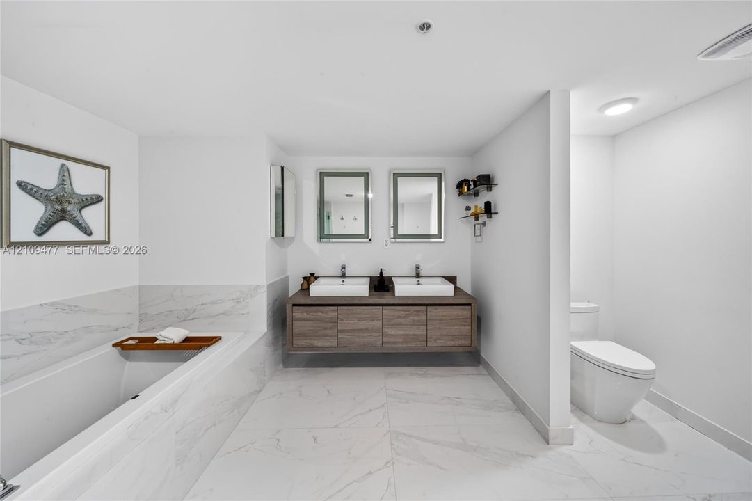 Bathroom featuring a wood-finish vanity with a rectangular vessel sink, integrated lighting mirror, stone-finish countertop, and large-format tile flooring