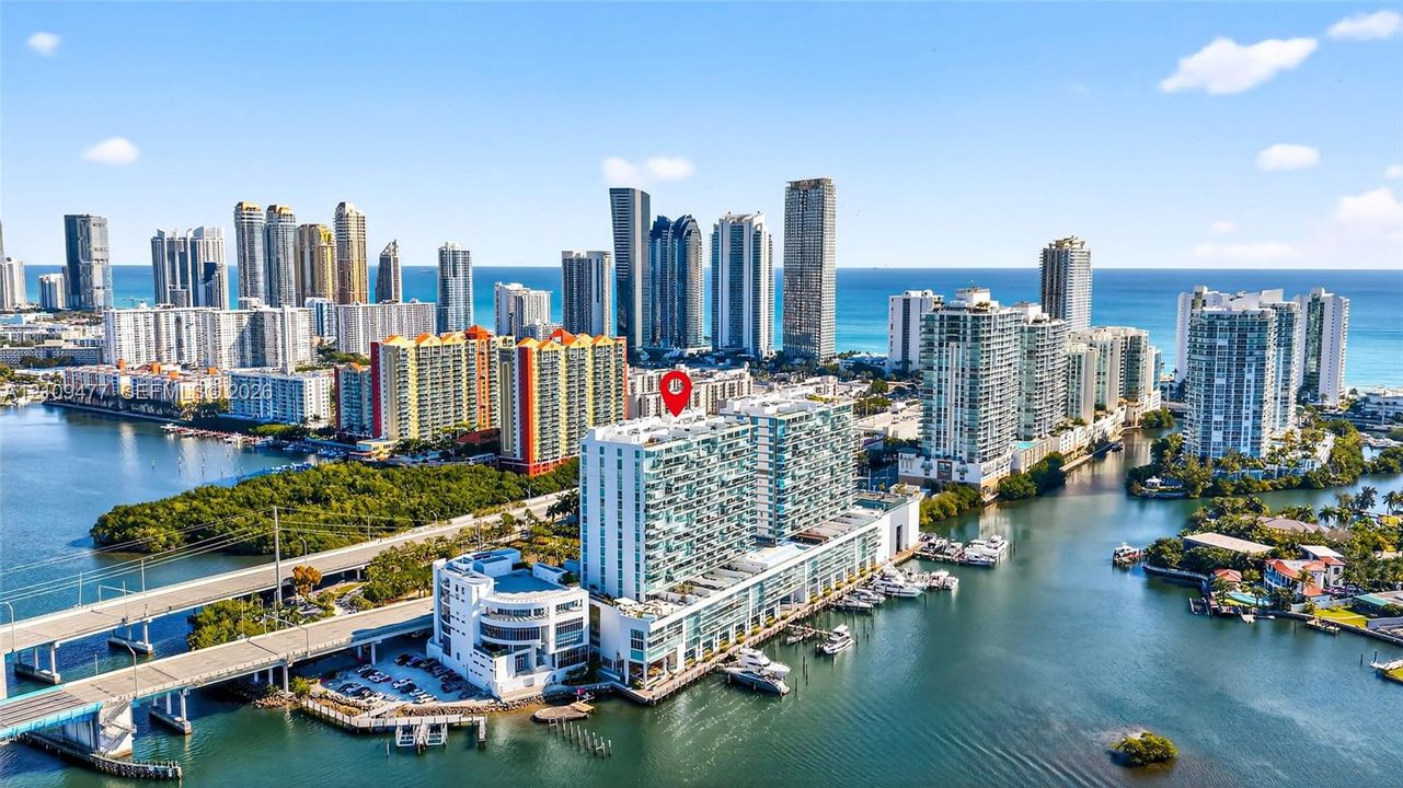 Aerial perspective of a high-rise residential building situated on the waterfront, featuring a private marina and balconies with glass railings