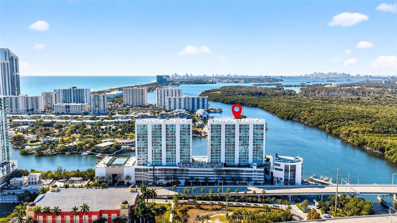 Aerial perspective of a high-rise residential building situated along a waterway, featuring coastal surroundings, expansive water access, and proximity to regional infrastructure