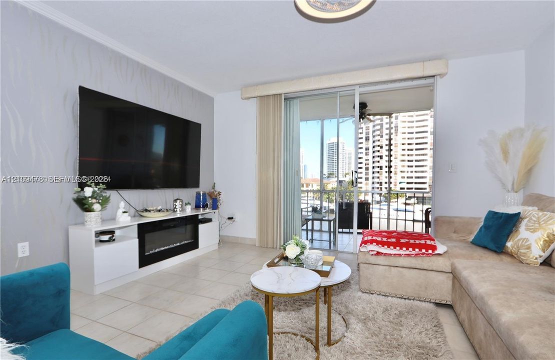Living room featuring tile flooring, built-in media console with integrated electric fireplace, textured accent wall, and floor-to-ceiling sliding glass doors opening to a balcony