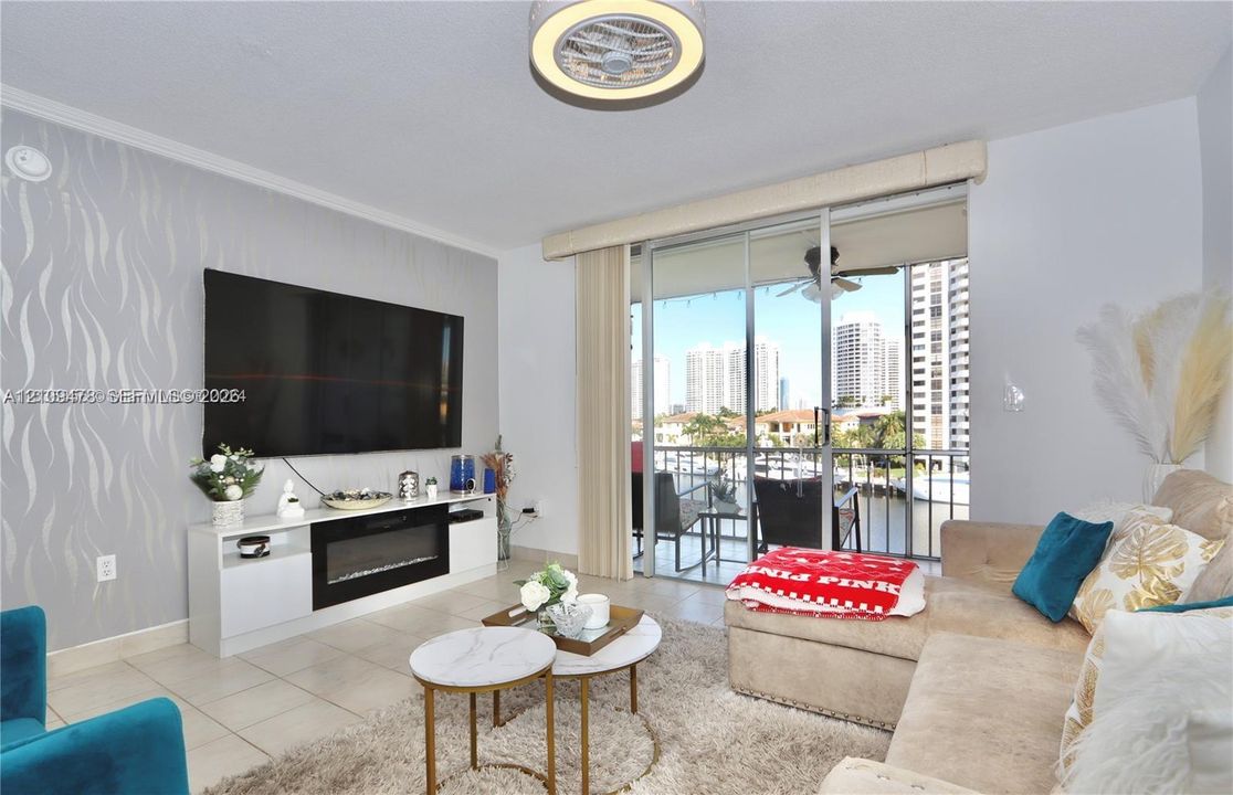 Living area featuring tile flooring, a wall-mounted fireplace, accent wallpaper, a contemporary circular ceiling light, and sliding glass doors with access to an outdoor balcony