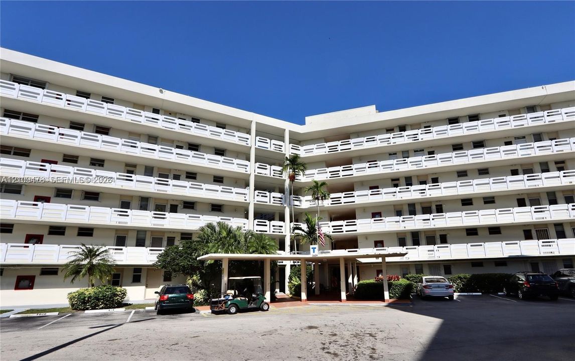 Multi-story building exterior featuring white concrete balconies with geometric railings and a covered porte-cochère entry