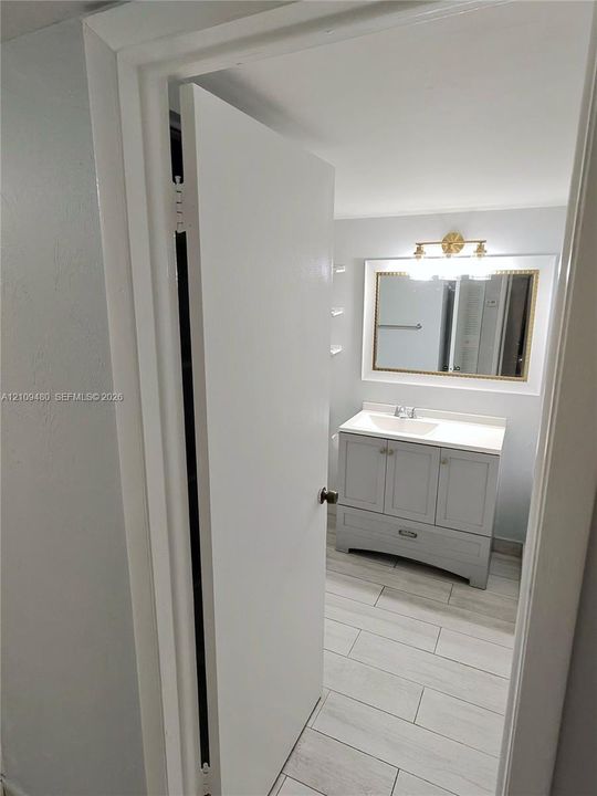 Bathroom featuring a grey vanity with a rectangular sink, stone-finish countertop, framed wall mirror, multi-bulb vanity light, and light-toned tile flooring