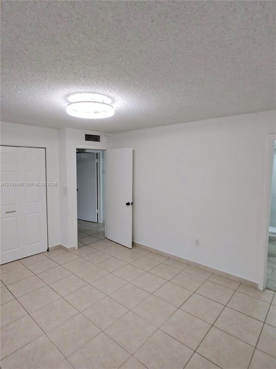Neutral tile flooring, textured ceiling, flush-mount circular lighting, and paneled closet doors