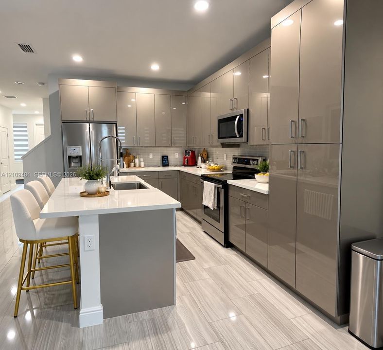 Kitchen featuring flat-panel cabinetry, quartz countertops, a kitchen island with a built-in sink, stainless steel appliances, and large-format porcelain tile flooring