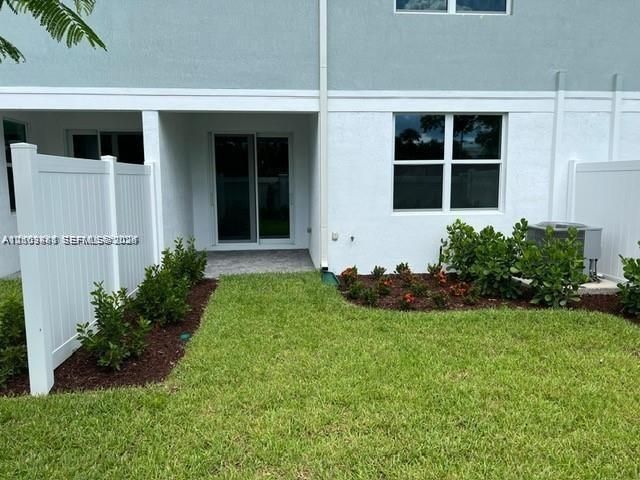 Exterior patio area featuring a white privacy fence, concrete paver flooring, managed landscaping, and sliding glass doors