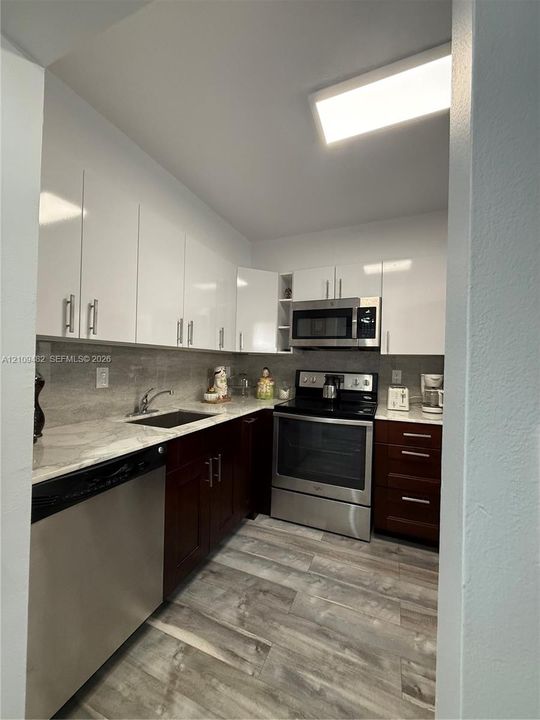 Kitchen featuring dual-tone cabinetry, stone-patterned countertops, stainless steel appliances, and wood-finish flooring