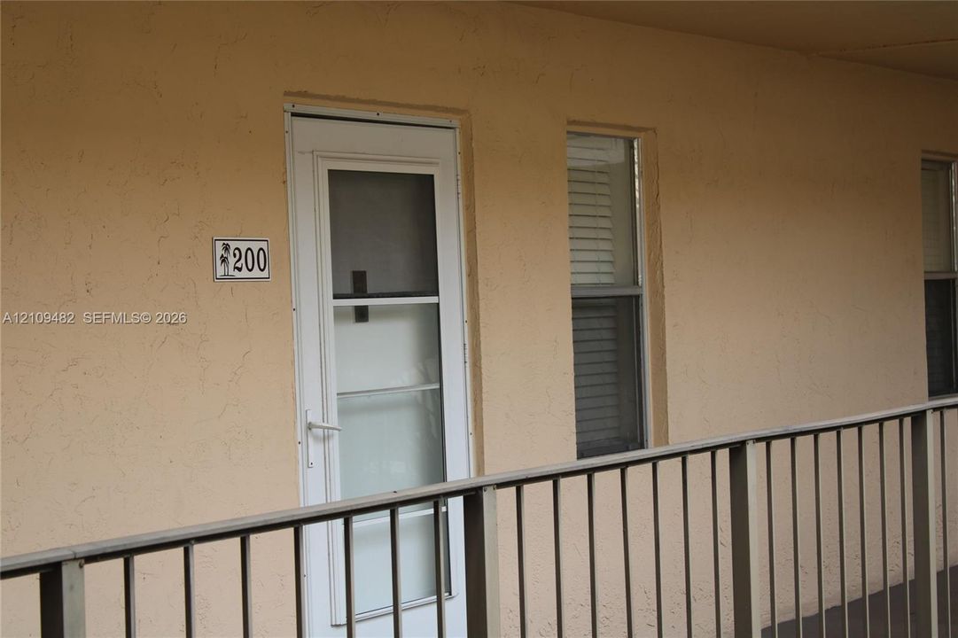 Stucco exterior featuring a white storm door with screen insert and metal railings