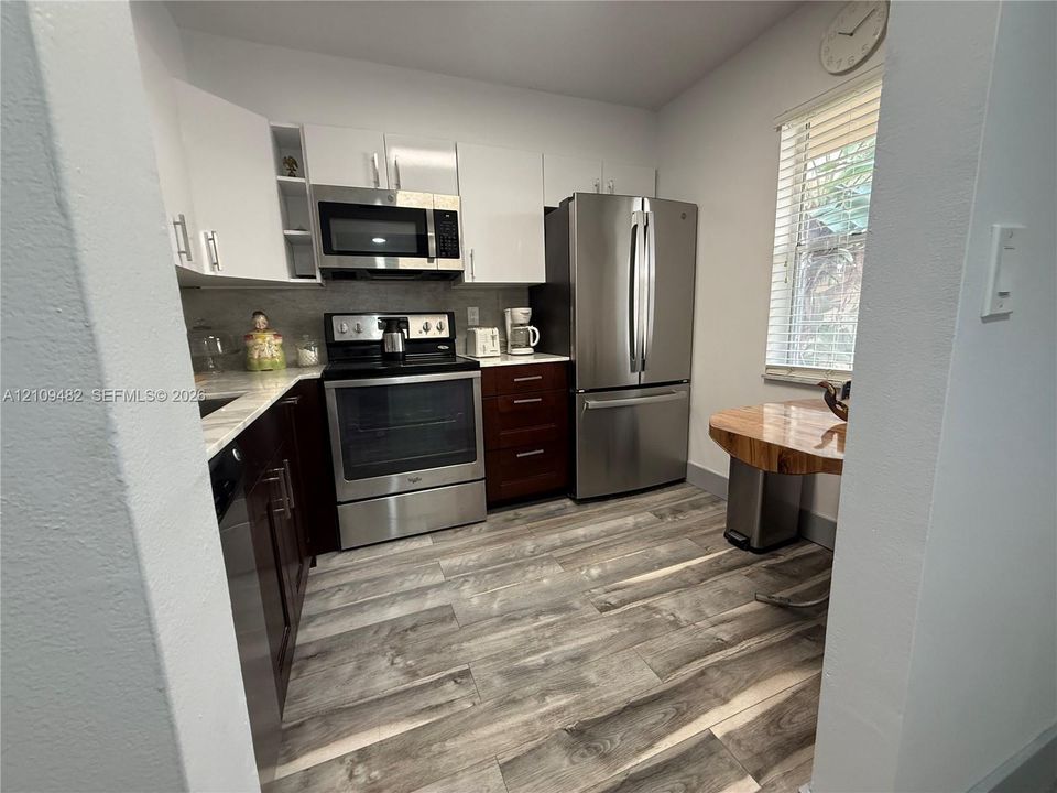 Kitchen featuring two-tone cabinetry, stainless steel appliances, wood-finish flooring, and horizontal blinds